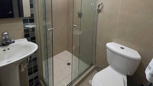 Een badkamer met een douchecabine van glas, een witte wastafel en een toilet.