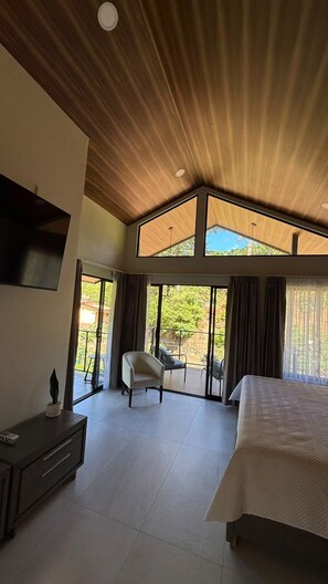 A modern bedroom with a large bed, a TV mounted on the wall, and a balcony with seating.