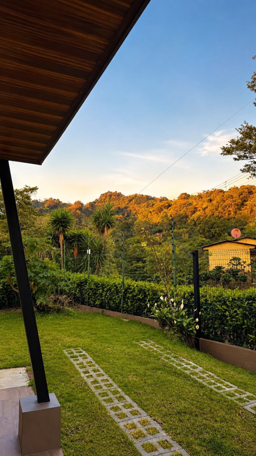 Un jardín bien cuidado con un camino empedrado, abundante vegetación y vistas a una colina con árboles.