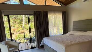 Ein modernes Schlafzimmer mit einem großen Bett, einer Sitzecke mit einem Sessel und Blick durch eine Glastür.