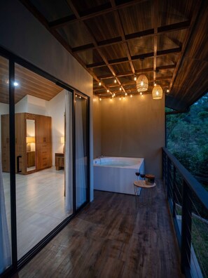A modern interior with a wooden floor, a large sliding glass door leading to a room with a wooden wardrobe, a bathtub, and a small table with glasses.