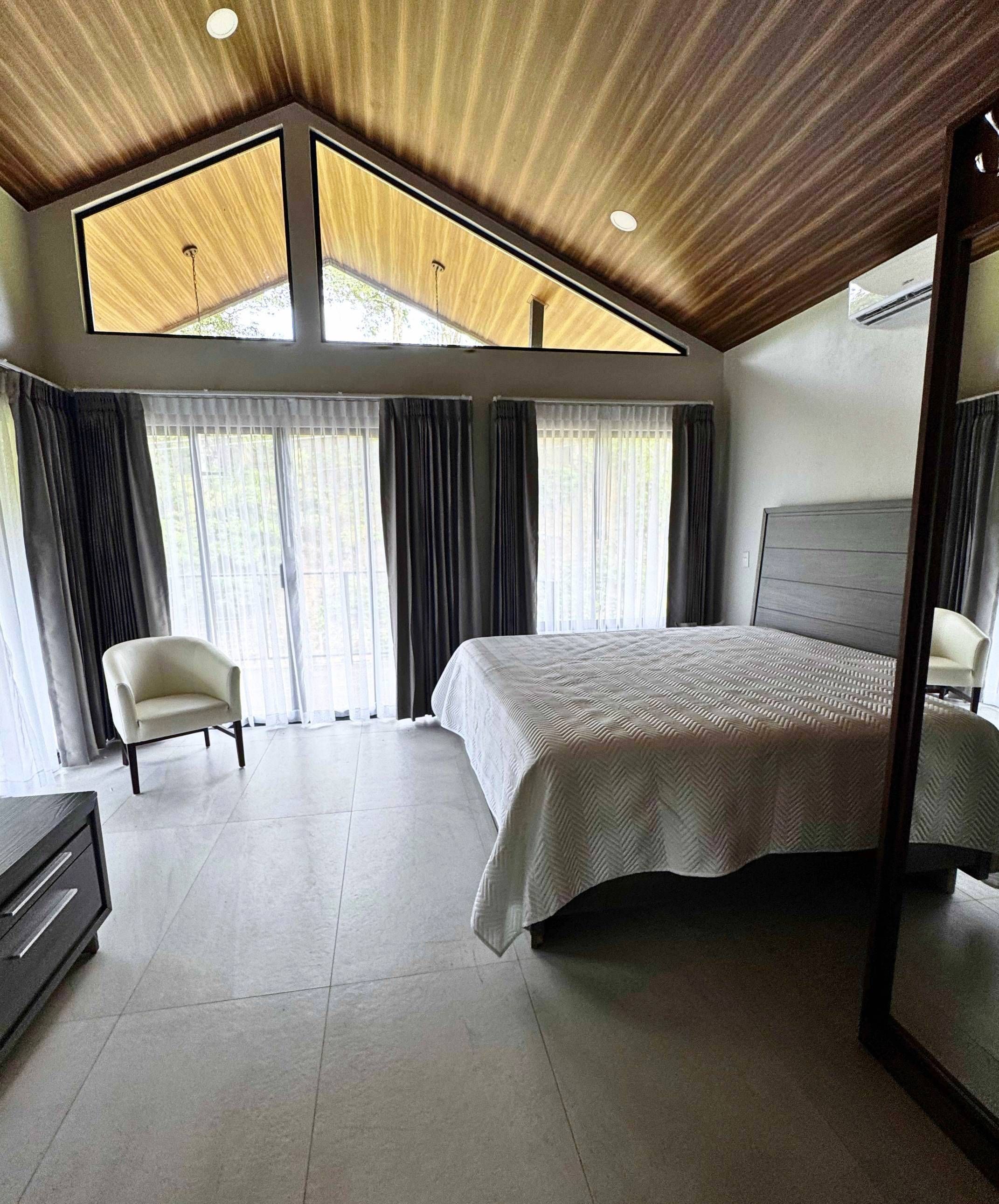 A modern bedroom with a large bed, a chair, and a mirror.