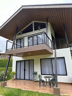 A modern two-story house with a balcony, large windows, and a patio area with outdoor furniture. - Alto Bosque. Mountain chalet with a private hot tub ⛰️🌿 (Berlín)