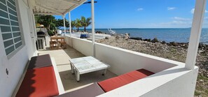 A covered outdoor seating area with a table and chairs, a grill, and a view of the beach and ocean. - Private Beachfront Estate w/ Infinity Pool (Santa Isabel)