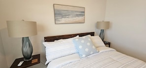 A neatly made bed with striped bedding, two bedside lamps, a remote control, and a framed picture on the wall.