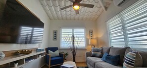 A living room with a ceiling fan, a blue armchair, a grey sofa, and a window with blinds.