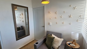 A hallway with a mirror, starfish wall decor, a grey sofa with cushions, a small table with a lamp, and a window with blinds. - Private Beachfront Estate w/ Infinity Pool (Santa Isabel)