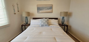 A bedroom with a bed, two nightstands, a lamp on each nightstand, a painting above the bed, and a window with blinds. - Private Beachfront Estate w/ Infinity Pool (Santa Isabel)