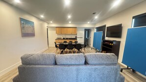 Un salon moderne avec un canapé gris, un coin repas avec une table et des chaises, une cuisine en arrière-plan et un téléviseur fixé au mur.