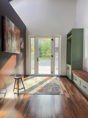 Ein Zimmer mit einer großen Glastür, die nach draußen führt, Holzboden, einem grünen Schrank und einem Teppich.