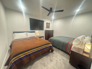 Ein Schlafzimmer mit einem Bett, einem Nachttisch mit Lampe, einem Schminktisch und einem Deckenventilator, sowie einem Fenster.