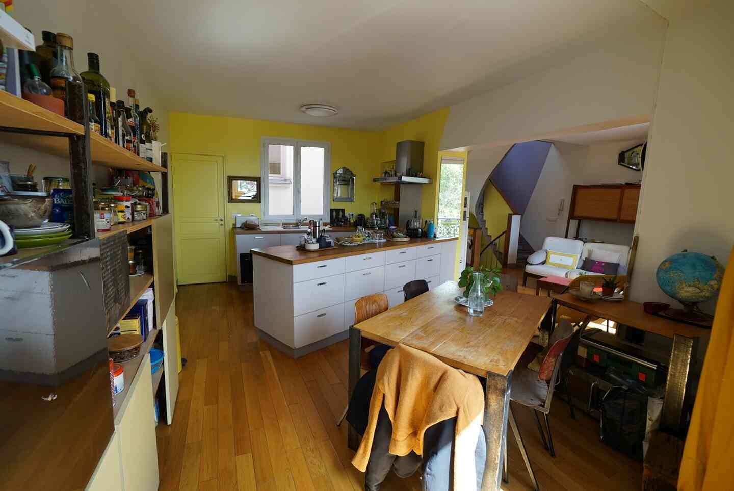 A compact kitchen with a central island, wooden flooring, and a dining area with a table and chairs.