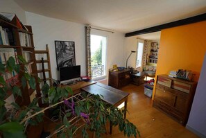 A room with a wooden desk, a computer, a bookshelf, a window with curtains, and a plant. - Bright apartment with a view of all of Paris, 5 rooms, 3 levels, feels like a house, Belleville (Paris)