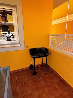 En lille balkon med et vindue, en sort metalstol og et hvidt gelænder.