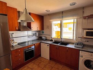 A kitchen with wooden cabinets, a built-in oven, a dishwasher, and a washing machine. - 4-room House in a secure complex with a pool and beaches just 5 minutes away (Alcalà de Xivert)
