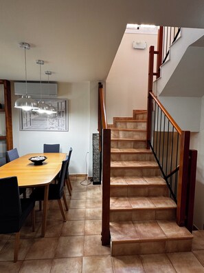 A dining area with a wooden table and chairs, a staircase with a wooden railing, and pendant lighting. - 4-bedroom house in a gated community with a pool and beaches just 5 minutes away (Alcalà de Xivert)