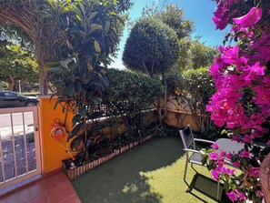 A patio with artificial grass, a chair, and a variety of plants including bougainvillea. - 4-room House in a secure complex with a pool and beaches just 5 minutes away (Alcalà de Xivert)
