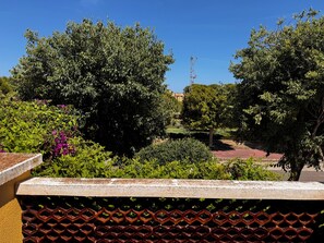 A balcony with a view of a garden, a metal fence, and a building in the background. - 4-room House in a secure complex with a pool and beaches just 5 minutes away (Alcalà de Xivert)