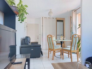 Un salon moderne avec un canapé, une table à manger, des chaises, un téléviseur et une plante suspendue.