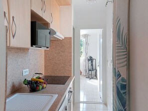 A kitchen with a microwave, fruit basket, and a view into a dining area with a fan. - Les Nouvelles Mirandas by Interhome (Saint Cyprien)