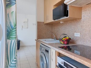 Une cuisine compacte équipée d’un four à micro-ondes, d’un évier et d’un panier de fruits.