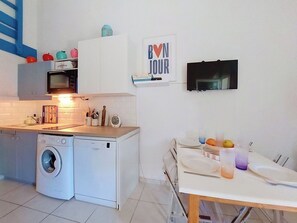 Eine kompakte Küche mit Waschmaschine, Mikrowelle und einem an der Wand befestigten Fernseher.