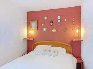Ein Bett mit weißen Leinentüchern, einem Holzkopfteil und einer roten Wand mit Dekoration und Wandleuchten.