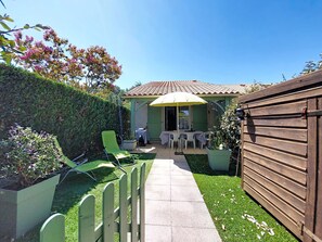 Eine Terrasse mit Tisch und Stühlen, ein Holzzaun und ein kleiner Garten mit Pflanzen und Rasen.