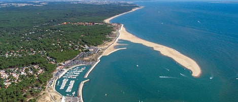 Vue aérienne d’une zone côtière avec une plage, un port de plaisance et des immeubles résidentiels.