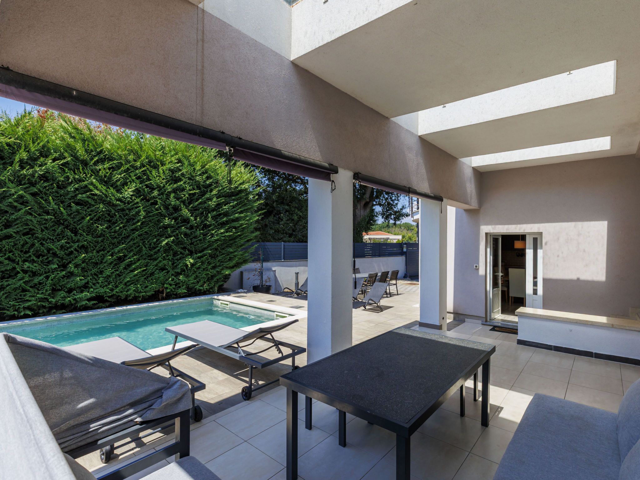 A modern outdoor patio with a pool, lounge chairs, and a covered seating area.