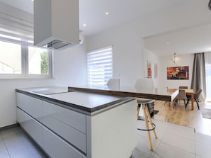 A modern kitchen with a central island, a dining area with a table and chairs, and a view of the outside through large windows. - Vacation home A.E.M by Interhome (Medulin/Šišan)