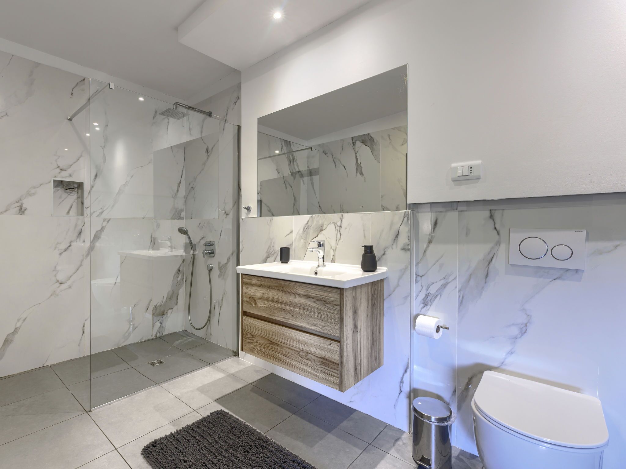A modern bathroom with a glass-enclosed shower, a wooden vanity, and a toilet.