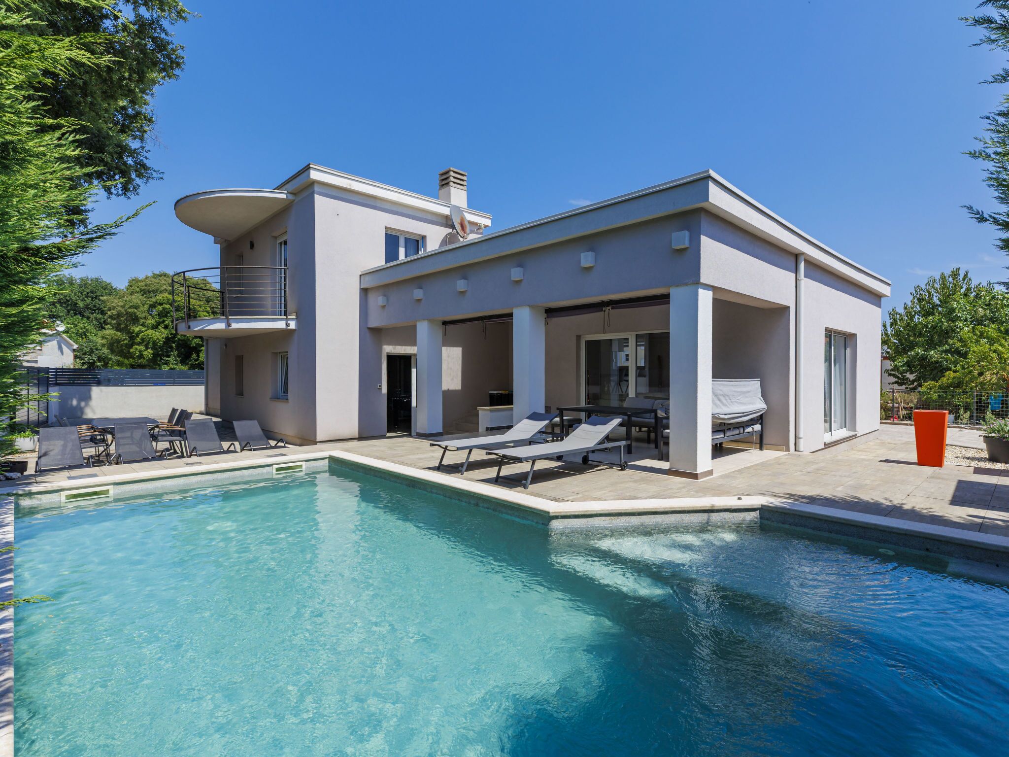 Una casa moderna de dos pisos con piscina y mobiliario de exterior.