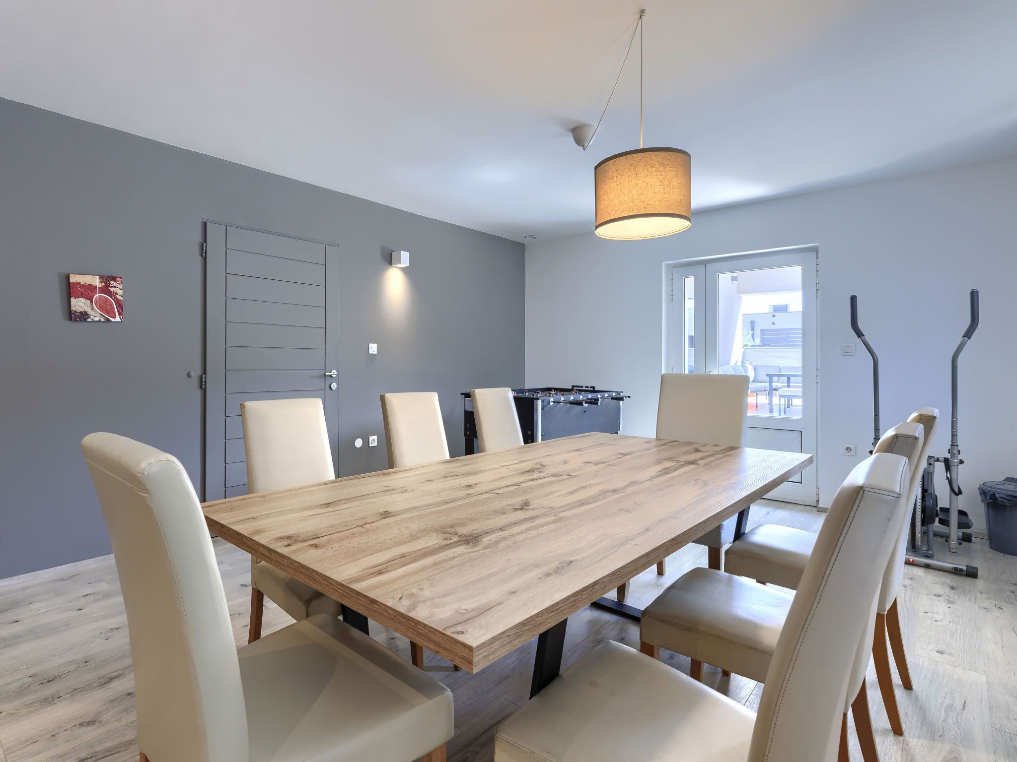 Une salle à manger moderne avec une table en bois, des chaises blanches et un luminaire suspendu.
