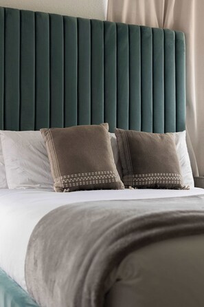 A bed with a dark green upholstered headboard, two pillows with a patterned trim, and a white pillow with a subtle design. - 4 Homes in One! | One Block to the Beach & Pier (San Diego)