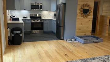 Una cocina moderna con gabinetes grises, electrodomésticos de acero inoxidable y piso de madera.