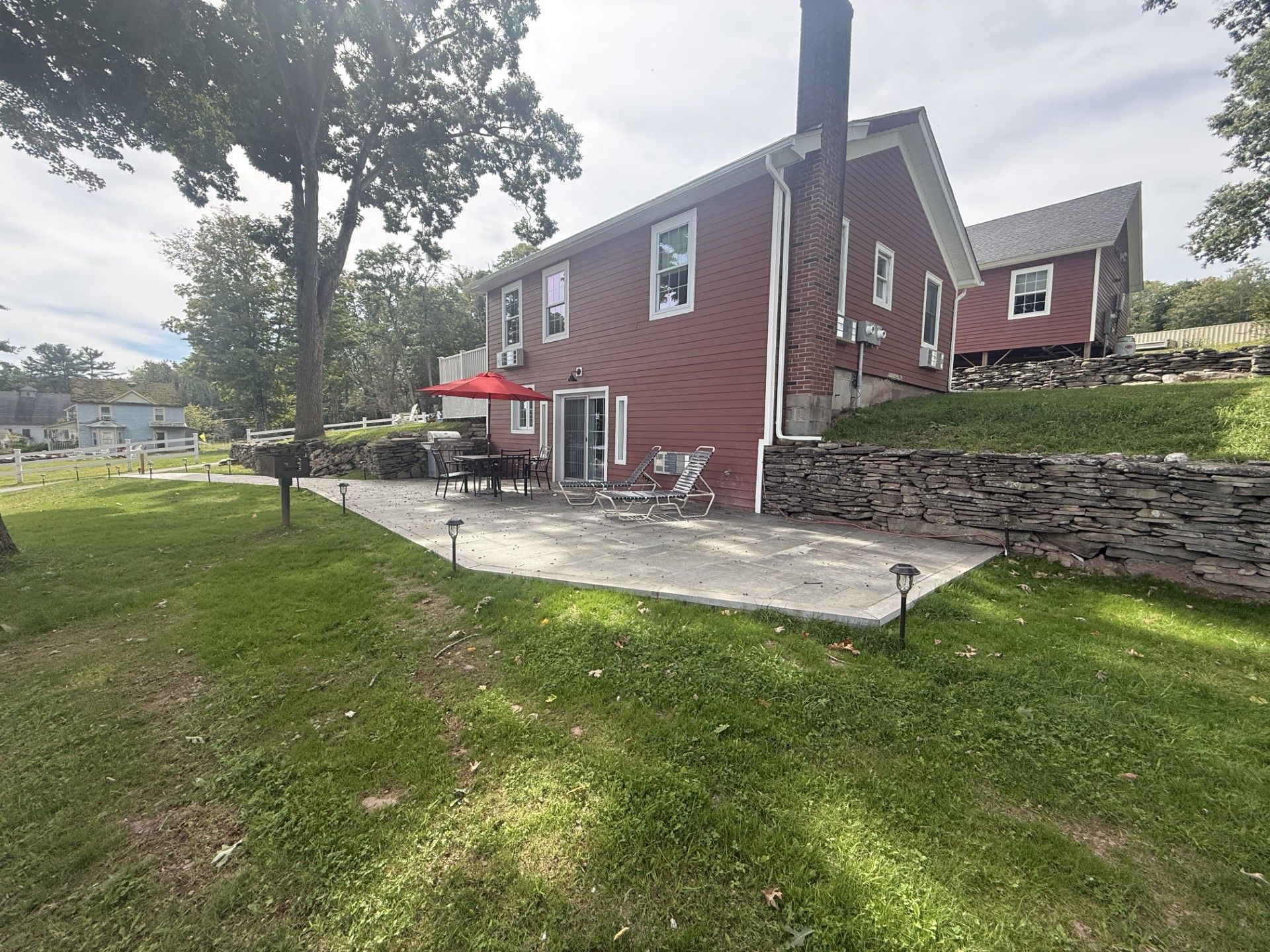 Una casa roja con un patio, mobiliario exterior y un muro de piedra.
