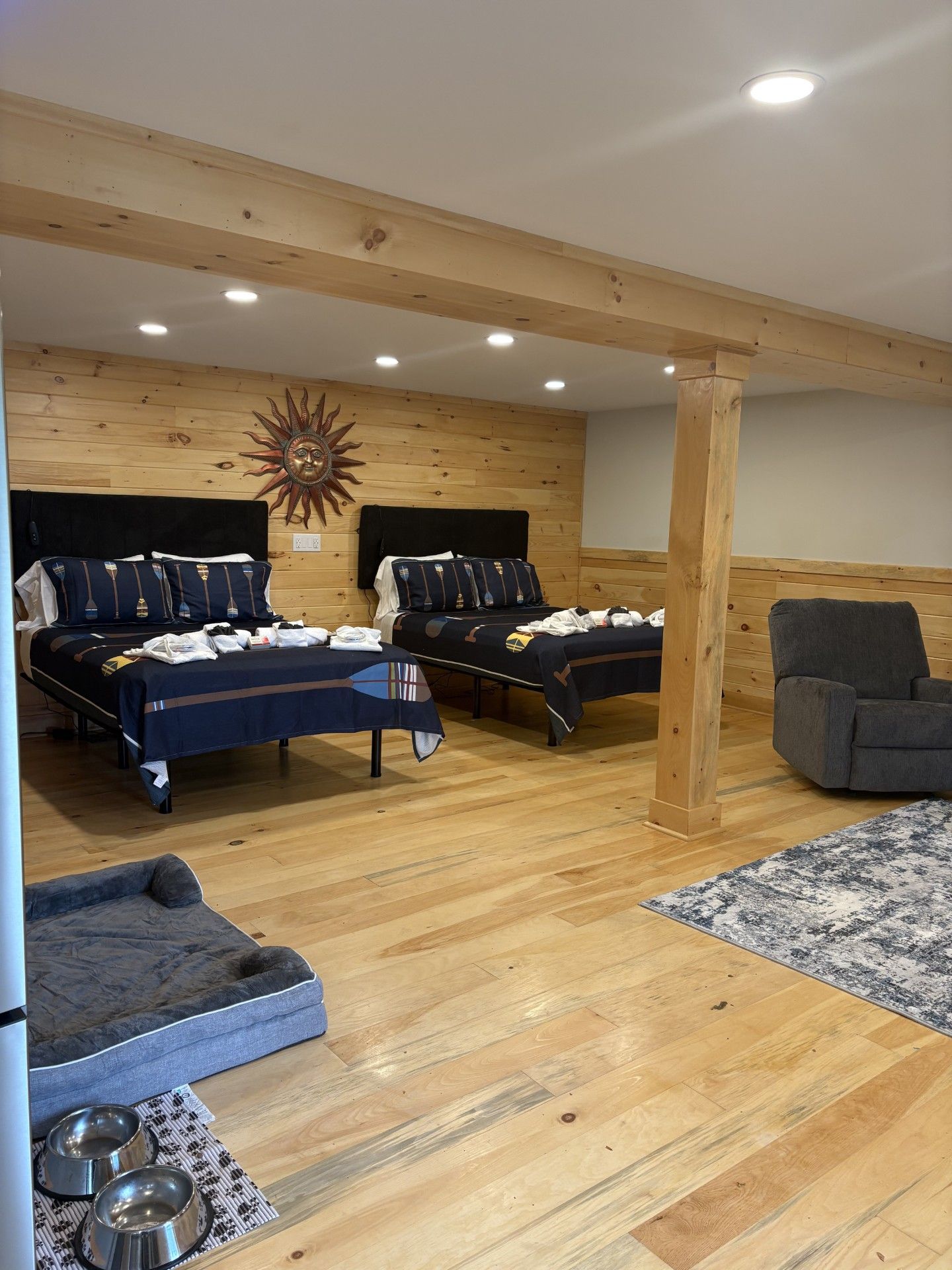 Una habitación con dos camas, techo de madera y un sillón gris.