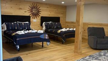 Una habitación con dos camas, techo de madera y un sillón gris.