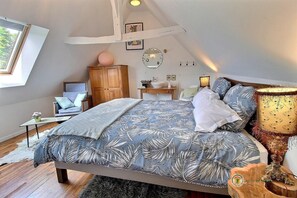 Une chambre à coucher avec un grand lit, une armoire en bois, une petite table, une table de chevet, une lampe et une fenêtre.