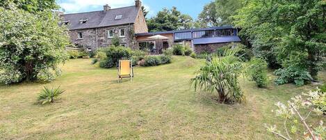 A stone building with a garden in front, a chair, and a small palm tree.