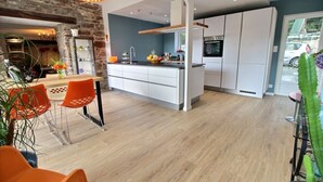 Eine moderne Küche mit weißen Schränken, einer zentralen Kochinsel und einem Essbereich mit orangefarbenen Stühlen.