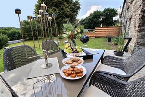 Un espace extérieur aménagé pour les repas, avec des chaises en osier, une table en verre, un barbecue et un luminaire décoratif.
