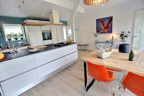 A modern kitchen with white cabinetry, a wooden island, and a dining area with orange chairs. - The Charm of the Two Rivers (BELLE ISLE EN TERRE)