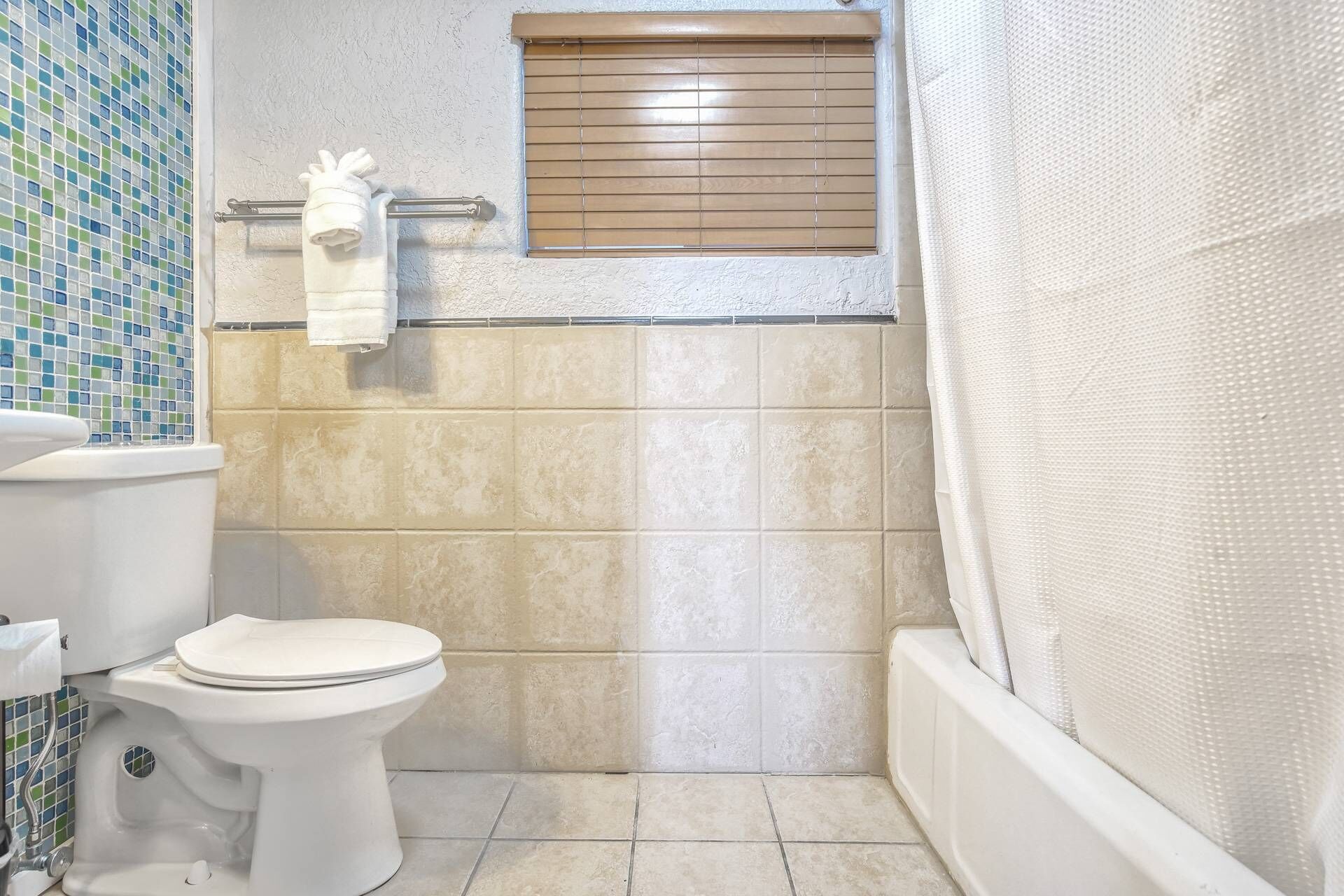 A bathroom with a toilet, a window with blinds, and a shower curtain.