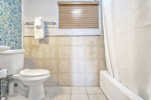 A bathroom with a toilet, a window with blinds, and a shower curtain. - San Ayre Court - The Green Room (1) (Colorado Springs)