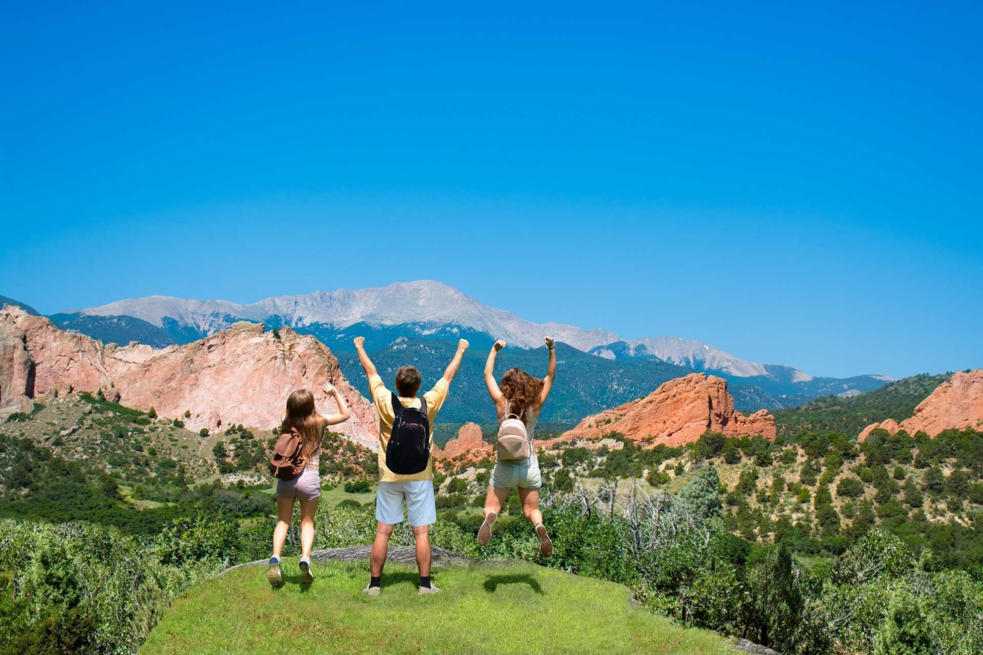 Three people standing on a grassy hill with a mountainous landscape in the background.