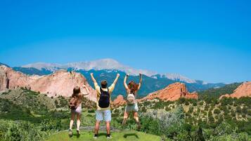 Three people standing on a grassy hill with a mountainous landscape in the background.