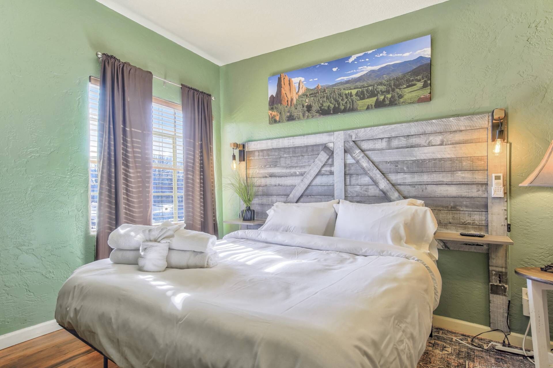 Une chambre à coucher avec un lit, des rideaux, un tableau, une table de chevet et une lampe.