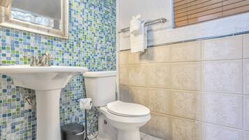 Un baño con un salpicadero de mosaicos, un lavamanos pedestal, un inodoro y un cubo de basura.